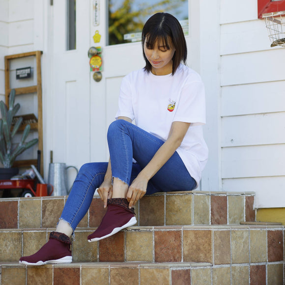 Red KAMON tabi shoes featuring a split-toe design, shown worn in a relaxed outdoor setting.
