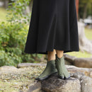 "Close-up of a person wearing U-ten x FLEECE Tabi Shoes in khaki, paired with a black midi skirt, standing on natural stone in an outdoor setting."