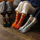 Three people sitting side by side wearing long Tabi Socks 'Nara Daibutsu' in black, orange, and dull blue — each featuring colorful Buddha face designs