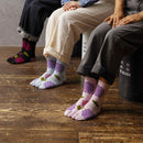 Three people sitting side by side wearing long Tabi Socks 'Ajisai' in black, blue, and pink — each featuring a purple hydrangea flower pattern with green leaves