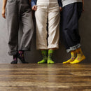 "Three people standing side by side wearing Tabi Socks 'Sankuzushi' in black, green, and yellow, with cuffed pants revealing the colorful designs"
