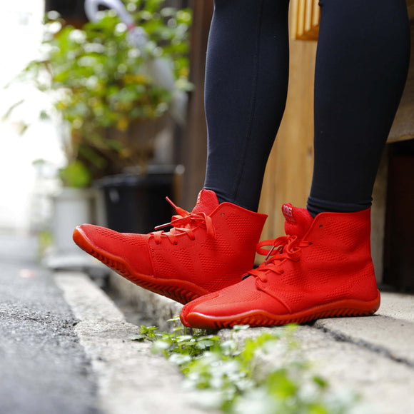 Lifestyle image of a person wearing red SPORTS JOG II tabi shoes while walking outdoors, showcasing the bold color and split-toe design.