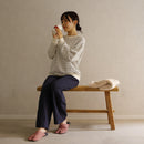 Lifestyle image of a person wearing KANOKO tabi slippers while sitting on a wooden bench in a calm, minimalist interior.