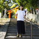"Person wearing MEISAI Tabi Shoes in green camouflage, styled with a white top and a long black skirt, standing on stone steps at a traditional Japanese shrine."