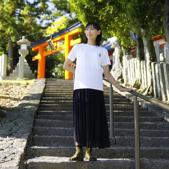 "Person wearing MEISAI Tabi Shoes in green camouflage, styled with a white top and a long black skirt, standing on stone steps at a traditional Japanese shrine."