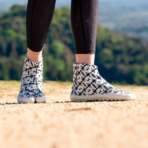 Outdoor side view of black Tabi Shoes "TIGRE" worn with black leggings on a dirt path.