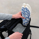 Packing view of blue Tabi Shoes "TIGRE" being placed into a black backpack, showing the patterned soles.